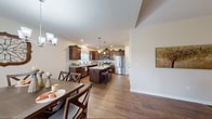 Located at 1551 Bellora Wy in Webster, NY, this single-floor home offers a thoughtfully designed layout with cohesive finishes throughout. Rich hardwood-style flooring flows through the main living areas, anchoring the open-concept design. The kitchen is a standout feature, showcasing rich dark cabinetry, granite countertops, stainless steel appliances including a gas range and French door refrigerator, and a central island with bar seating. A window above the sink allows natural light to fill the space. The adjacent dining area connects seamlessly to the kitchen and offers sliding glass door access to an outdoor deck with open views. The living room is warm and inviting, with vaulted ceilings, ceiling fan, and hardwood-style flooring. A wide, well-lit hallway leads to the private quarters. The primary bedroom is a serene retreat, highlighted by an elegant tray ceiling with crown molding and ceiling fan. The en-suite bathroom features a glass-enclosed walk-in shower, tile flooring, dual-sink vanity with dark wood cabinetry, and access to a spacious walk-in closet with wire shelving. The dedicated laundry room includes upper cabinetry for additional storage. The home's neutral palette and clean architectural lines create a comfortable, move-in ready environment.