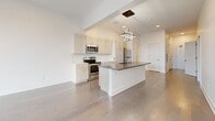 Located on Elmwood Avenue in Buffalo, NY, this thoughtfully designed 2-bedroom, 3-bathroom residence offers a clean, modern aesthetic throughout. Wide-plank hardwood flooring flows continuously through the main living areas, anchoring the bright, open-concept layout. The kitchen serves as the centerpiece of the space, featuring light wood cabinetry, stainless steel appliances, and a substantial island with a dark countertop and an eye-catching geometric pendant light fixture above — ideal for both meal preparation and casual dining. A hallway with frosted-glass panel doors leads seamlessly from the entry toward the living and sleeping areas. The primary bedroom is a well-proportioned retreat with large windows that invite ample natural light, complemented by a dedicated walk-in closet outfitted with wire shelving and hanging rods for organized storage. The second bedroom includes a built-in double sliding-door closet. Three bathrooms offer contemporary finishes, including large-format tile flooring, dark wood floating vanities with white countertops, and a tiled walk-in shower in the primary bath. A half bath with a frosted privacy door provides added convenience. Throughout the residence, recessed lighting, clean white walls, and modern hardware contribute to a cohesive, refined atmosphere.