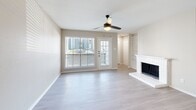 This single-floor residence offers a thoughtfully designed layout with modern finishes and functional living spaces throughout. The open living area serves as the heart of the home, anchored by a white brick fireplace with a classic mantel and flanked by built-in shelving — an ideal combination of warmth and practical storage. Light wood-style flooring flows seamlessly throughout, complementing the neutral, warm-toned walls. A ceiling fan provides comfort overhead, while large windows and a glass-paneled exterior door invite natural light and outdoor views into the space.

The kitchen is efficiently designed with a galley-style layout, featuring white upper cabinetry, gray lower cabinetry, white countertops, and a full suite of stainless steel appliances including a refrigerator, electric range, microwave, and dishwasher. A pass-through counter connects the kitchen to the living area, enhancing the open feel.

The bedrooms are comfortably sized, each with ceiling fans, ample natural light, and generous closet space — including a walk-in closet in the primary bedroom. The primary bedroom also offers direct access to an en-suite bathroom. The bathrooms are finished with gray vanity cabinetry, white countertops, and a tub-shower combination with black hardware accents. A dedicated in-unit laundry room houses a full-size top-loading washer and dryer.