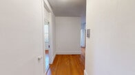 Located at 11 Tetlow St in Boston's Fenway neighborhood, this one-bedroom, one-bathroom unit offers a practical and well-laid-out single-floor living space. Warm hardwood flooring runs throughout the main living areas, hallway, and bedroom, lending a classic, cohesive feel to the interior. Crisp white walls and clean baseboards contribute to a bright, neutral aesthetic throughout.

The living room is generously proportioned, featuring multiple windows that allow ample natural light to fill the space. A set of traditional wooden double doors with decorative molding connects the living room to the rest of the unit, adding a charming architectural detail. The bedroom is a comfortable size, fitted with a classic cast-iron radiator and windows on two walls that bring in abundant daylight.

The kitchen features warm oak cabinetry, a coil-top electric range, and light countertops. A window over the counter area provides natural ventilation and light. The floor transitions to tile in this room. The bathroom continues the tiled theme with square wall tiles, mosaic floor tiles, and a bathtub with a window for natural light. A central hallway connects all rooms efficiently, and two closets provide practical storage. The unit includes an intercom panel near the entry.