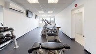 Located at 1 Campbell Ave in West Haven, Connecticut, this fitness center offers a comprehensive, single-floor workout facility designed to support a wide range of exercise needs. The space is laid out with distinct functional zones, each tailored to a specific type of training.

The cardio area is lined with treadmills and stair climbers positioned along a windowed wall, allowing natural light to fill the room and providing outside views during workouts. Multiple wall-mounted televisions are installed to keep members engaged during cardio sessions. Nearby, a row of stationary bikes and additional cardio equipment occupies its own dedicated section, also benefiting from natural light through exterior windows.

The strength training area features a well-stocked dumbbell rack with a full range of free weights, complemented by a large wall mirror that enhances the sense of space and allows for proper form checks. An adjustable workout bench is also available. A stability ball and additional functional training accessories round out the equipment available in this zone.

Throughout the facility, durable dark rubber flooring provides a safe, cushioned surface suited for all types of exercise. The space is finished with a dropped tile ceiling outfitted with recessed panel lighting, maintaining a bright and clean atmosphere. The facility is branded with "Activeline" signage visible on the glass entry doors, presenting a professional and welcoming environment.