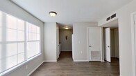 This 2-bedroom, 1-bathroom single-floor unit offers a straightforward and functional layout designed to maximize every square foot of its compact footprint. Dark wood-look flooring runs consistently throughout the space, providing a cohesive and low-maintenance foundation that complements the neutral gray and white color palette on the walls and trim.

The living room serves as the central gathering area, featuring a large window fitted with blinds that allows natural light to brighten the space. A hallway connects the main living area to the kitchen, bedrooms, and bathroom. The galley-style kitchen is equipped with a white electric range, dual rows of warm-toned wood cabinetry, and light countertops on both sides, making efficient use of the narrow layout.

Both bedrooms feature the same dark flooring and neutral walls, with windows that bring in natural light. Each bedroom includes a double-door closet with chrome hardware, offering practical built-in storage. The primary bedroom provides a comfortable and functional space for rest and relaxation.

The bathroom is fitted with a standard tub-shower combination, a toilet, and towel bars, maintaining the same clean, no-frills aesthetic found throughout the unit. A hallway connects all rooms efficiently, completing this well-organized and move-in-ready layout.