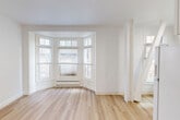 Located at 1030 Post St in San Francisco's Lower Nob Hill neighborhood, this efficiently designed studio offers a thoughtful layout across a single floor. The main living area is highlighted by a charming bay window that draws in abundant natural light, illuminating the crisp white walls and light-toned hardwood flooring throughout. A baseboard heating unit beneath the bay window ensures year-round comfort, while the open feel of the space makes it feel airy and welcoming.

A dedicated closet with sliding doors provides practical built-in storage, complemented by an electrical panel discreetly integrated into the wall. The kitchen is well-appointed with white cabinetry, a full-size refrigerator, an electric range, and a sink — all finished in a clean, cohesive white palette that enhances the sense of brightness. A window in the kitchen allows for additional natural light and ventilation.

The bathroom features a full soaking tub and shower combination, finished with clean white tiled walls accented by subtle horizontal detailing and brushed gold hardware, lending a refined touch to the utilitarian space. Throughout the unit, consistent light wood flooring ties each area together seamlessly, creating a uniform and polished aesthetic ideal for urban living in the heart of San Francisco.