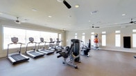 This fitness center offers a clean, well-organized workout environment designed to support a full range of exercise routines. The space is bathed in natural light, courtesy of large windows along multiple walls that create an open, inviting atmosphere. Ceiling fans are positioned throughout to ensure comfortable airflow during workouts.

The cardio zone is prominently featured and includes a row of treadmills and elliptical machines, all positioned to take advantage of the natural light streaming in from the large windows. Strength training is well represented with a multi-function weight machine for targeted resistance exercises. A stationary bike adds to the variety of cardiovascular options available.

Complementing the machines, a set of stability and exercise balls in varying sizes is neatly organized along the wall, providing tools for core training and flexibility work. The flooring is a durable, gym-appropriate surface suited for both equipment use and floor exercises.

The room features crown molding and recessed lighting, giving the space a polished, well-maintained appearance that elevates the overall experience. The neutral color palette and abundant natural light contribute to an energizing yet comfortable environment, making this fitness center a functional and appealing destination for daily exercise.