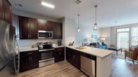 Located at Alston Station Square on Mill Road in Ronkonkoma, NY, this thoughtfully designed single-floor residence offers a seamless blend of modern style and practical living. The open-concept kitchen is a standout feature, showcasing rich dark-espresso cabinetry, granite countertops, a classic subway tile backsplash, and a full suite of stainless steel appliances including a refrigerator, range, microwave, and dishwasher. Pendant lighting over the peninsula adds a refined touch, while the kitchen flows naturally into the living and dining areas. The living room is bright and welcoming, with a door providing access to a private balcony that brings in natural light. Wood-style flooring runs throughout the main living spaces, lending warmth and continuity. The bedroom is carpeted and serene, offering ample space and natural light through large windows with custom drapery. The bathroom is cleanly finished with light tile flooring and a tub-shower combination. A convenient in-unit stacked washer and dryer is tucked into a dedicated closet, adding everyday practicality. Built-in shelving and generous storage throughout complete this well-appointed residence.