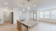 This thoughtfully designed 1-bedroom, 1-bathroom residence offers a bright and modern living experience across a single floor. The open-concept layout seamlessly connects the kitchen and living room, creating a spacious, airy feel enhanced by recessed lighting and an abundance of natural light from multiple windows. Light-toned hardwood-style flooring flows throughout the main living areas, adding warmth and continuity to the space.

The kitchen is a standout feature, showcasing a large central island with a granite countertop, undermount sink, and pendant lighting overhead. Taupe shaker-style cabinetry extends to the upper walls, providing ample storage, while stainless steel appliances — including a refrigerator and dishwasher — complete the modern aesthetic. A subway tile backsplash adds a clean, polished touch.

The living room benefits from a wall of windows and a private entry door, inviting natural light and outdoor views. The bedroom is generously sized, fitted with plush carpeting, a ceiling fan, and windows that frame neighborhood views. A dedicated closet provides excellent storage.

The bathroom is elegantly finished with a dual-sink granite vanity, gray cabinetry, and a glass-enclosed walk-in shower with tile surround. Additional conveniences include an in-unit laundry area, completing this well-rounded and move-in-ready residence.