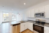 This well-appointed 2-bedroom, 2-bathroom residence is thoughtfully designed to maximize functionality and comfort across a single floor. The open-concept living, dining, and kitchen area serves as the heart of the home, featuring light hardwood-style flooring, recessed lighting, and large windows that invite abundant natural light. The kitchen is equipped with stainless steel appliances — including a refrigerator, range, microwave, and dishwasher — paired with white shaker-style cabinetry, dark granite-look countertops, and a peninsula with a built-in sink, ideal for both cooking and casual dining. A wall-mounted mini-split unit provides climate control throughout the main living space. Both bedrooms are bright and airy, each featuring large windows with views of the surrounding neighborhood and baseboard heating. The primary bedroom offers a generous footprint and closet access. Three closets in total provide ample storage, including a walk-in closet with wire shelving. The two bathrooms are finished in a clean, modern style with white cabinetry, bright vanity lighting, and hardwood-style flooring. A dedicated laundry area houses a stacked washer and dryer unit for added convenience.