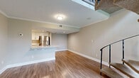 Located at 7950 Shoals Drive in Orlando, Florida, this two-floor residence offers a thoughtfully designed open-concept layout finished with warm hardwood-style flooring and neutral-toned walls throughout. Crown molding and textured ceilings add a classic architectural touch to the main living areas.

The main level centers around a generous living area that flows seamlessly into the kitchen. The kitchen is equipped with stainless steel appliances, including a refrigerator, range, microwave, and dishwasher, complemented by white cabinetry and a peninsula with a built-in sink — ideal for casual dining or food preparation. Recessed lighting illuminates the kitchen workspace, while natural light filters in through well-placed windows.

A standout architectural feature of the space is the carpeted spiral staircase with a sleek black metal railing, connecting the main level to the upper floor. The open volume above the staircase enhances the sense of height and airiness in the living area. The front entryway provides a welcoming transition into the home, with a window offering views of the surrounding greenery.

A full bathroom with a tub-shower combination and clean white finishes serves the upper level. The overall ambiance throughout is bright, clean, and functional, making this a well-appointed two-floor residence in Orlando.
