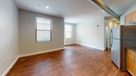 Located at 26 Portland St in Worcester, MA, this single-floor unit offers a thoughtfully designed layout with a clean, modern aesthetic throughout. Rich hardwood flooring flows seamlessly across the living areas, bedrooms, and hallways, lending warmth and continuity to the space.

The open kitchen is a standout feature, outfitted with warm-toned maple cabinetry, dark granite countertops, and a full suite of stainless steel appliances including a refrigerator, electric range, built-in microwave, and dishwasher. Exposed industrial-style ductwork along the ceiling adds a loft-inspired character to the kitchen and living area.

The living space is bright and open, with multiple windows dressed with horizontal blinds that allow for natural light. The neutral gray-toned walls create a versatile backdrop throughout. Multiple rooms offer flexibility for use as bedrooms or additional living space, each with windows and access to closet storage. A frosted-glass interior door adds a refined architectural detail to one of the rooms.

The bathroom is finished with tile flooring and includes a full tub/shower combination, a vanity with sink, and a round mirror. The unit also features recessed lighting and visible HVAC infrastructure, reflecting its updated, functional design within an urban Worcester setting.