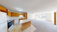 This 2-bedroom, 1-bathroom unit in West Allis, Wisconsin offers a practical and comfortable single-floor layout. The open-concept kitchen flows seamlessly into the living room, creating a spacious, connected feel. The kitchen is well-equipped with warm honey-oak cabinetry offering generous storage, a peninsula with a light countertop ideal for additional prep space or casual dining, and white appliances including a refrigerator, range, and dishwasher. Tile-style flooring adds durability in the kitchen area. The living room is carpeted and bathed in natural light, anchored by a large sliding glass door that opens to a private balcony with views of the surrounding neighborhood. A track lighting fixture overhead adds functional illumination. The full bathroom features an oak vanity with a light countertop and tile-style flooring, conveniently accessible from the main hallway. Both bedrooms are carpeted with neutral walls and warm wood trim. The primary bedroom is a comfortable size and is accompanied by a dedicated closet with built-in shelving and a hanging rod. The second bedroom receives natural light through a window with blinds. A closet with wire shelving provides additional storage within the unit.