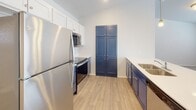 This single-floor home on Tallgrass Avenue in Sioux Falls, South Dakota offers a well-designed layout with a clean, modern aesthetic throughout. The open-concept kitchen and living area is a standout feature, boasting soaring vaulted ceilings that lend an airy, expansive feel to the space. The kitchen is outfitted with stainless steel appliances, including a refrigerator, range, and microwave, complemented by a two-tone cabinetry scheme pairing crisp white upper cabinets with bold navy lower cabinets and a pantry unit. Light wood-look flooring runs through the kitchen and connecting areas, adding warmth. Pendant lighting over the kitchen peninsula enhances both function and style.

The bedrooms feature neutral-toned carpeting and blinds-equipped windows that allow natural light while maintaining privacy. A hallway connects the sleeping quarters to a bathroom featuring a navy vanity with a sink and wood-look flooring. An adjacent built-in shelving unit provides organized storage, and a dedicated laundry closet houses a full-size top-load washer and dryer. The overall palette throughout the home is light and neutral, creating a bright, cohesive atmosphere.
