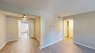 Located on Duck Pond Circle in Morrisville, NC, this single-floor residence offers a well-organized layout designed for comfortable everyday living. The living room serves as the centerpiece of the home, anchored by a striking full-height brick fireplace flanked by two large windows that flood the space with natural light and offer views of the surrounding neighborhood. Hardwood-style flooring runs throughout the main living and transition areas, lending a clean, cohesive aesthetic.

The kitchen is outfitted with crisp white shaker-style cabinetry, brushed gold hardware, light quartz countertops, and a stainless steel undermount sink with a coordinating gold-tone faucet — a modern and functional workspace. A ceiling fan in the adjacent dining or hallway area aids in air circulation throughout the common spaces.

The bedrooms feature plush carpeting and are complemented by well-sized closets with built-in shelving. One bedroom connects to a dedicated bathroom that includes a tiled shower-tub combination and hardwood-style flooring, providing a practical and tidy space. Additional rooms offer neutral wall tones and generous natural light, making them versatile for various uses. The floor plan flows logically from room to room, creating a practical and comfortable living environment.