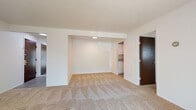 This single-floor residence offers a practical and comfortable layout spread across several connected rooms. The living area is generously sized, featuring neutral-toned wall-to-wall carpeting and a large sliding glass door fitted with vertical blinds that allows abundant natural light to fill the space. Structural beam details along the ceiling add subtle architectural character to the room.

The galley-style kitchen is efficiently designed with white cabinetry lining both sides, granite-patterned countertops, stainless steel appliances including a refrigerator and dishwasher, and a deep undermount sink. Light wood-look flooring runs throughout the kitchen, providing a clean contrast to the surrounding cabinetry.

The bedroom is a well-proportioned carpeted room with a window that brings in natural light, along with direct access to a full bathroom. The bathroom features wood-look flooring, a white vanity with ample counter space, a full-wall tiled tub and shower combo, and a framed mirror. A separate hallway bathroom is also accessible from the main living area, sharing a similar clean, tiled aesthetic. Overall, the unit presents a neutral, move-in-ready environment with consistent finishes throughout.