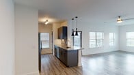 This well-appointed single-floor unit showcases a thoughtfully designed open-concept layout that seamlessly connects the kitchen and living areas. The kitchen is a standout feature, equipped with sleek dark cabinetry, stainless steel appliances including a range, microwave, refrigerator, and dishwasher, complemented by granite countertops and a stylish subway tile backsplash. A peninsula with pendant lighting overhead serves as both a functional workspace and casual dining area. Multiple windows throughout flood the living spaces with natural light, while light-toned luxury vinyl plank flooring adds warmth and continuity across the main areas.

The open living room offers generous proportions, highlighted by a ceiling fan and large windows that bring in abundant daylight and views of the surrounding area. The bedroom features plush carpeting and a well-sized window that adds to the bright and airy ambiance of the room.

The bathroom is a particularly elegant touch, featuring a deep soaking tub surrounded by large-format marble-look tile that extends from floor to ceiling, lending a luxurious, spa-like atmosphere. Clean white walls and crisp trim throughout the unit create a fresh, modern aesthetic that is both functional and inviting.
