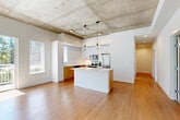 Located at 2681 Tagore Ave NE in Redmond, WA, this two-bedroom, two-bathroom residence offers a well-designed single-floor layout with a cohesive modern aesthetic throughout. The open-concept kitchen and living area serves as the heart of the home, distinguished by striking exposed concrete ceilings and warm hardwood-style flooring. The kitchen is outfitted with stainless steel appliances — including a refrigerator with ice and water dispenser, electric range, built-in microwave, and dishwasher — complemented by two-tone cabinetry featuring white upper cabinets and natural wood lower cabinets, white quartz countertops, a subway tile backsplash, and a central island. A window brings natural light into the living area, which also features exposed concrete columns that add an industrial character. Both bedrooms offer carpeted flooring, with the primary bedroom providing a comfortable, well-proportioned retreat. The four closets, including walk-in options with wire shelving systems, provide generous storage throughout. The two bathrooms are finished with wood-toned vanities and white quartz countertops. A hallway connects the private areas of the home, and a balcony extends the living space outdoors.