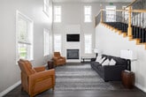 Located at 600 Pioneer Rd in Rexburg, Idaho, this two-floor community space offers a well-rounded amenity experience across a generously sized footprint. The main floor greets visitors with a striking double-height entryway, featuring soaring ceilings, large transom windows that flood the area with natural light, and an elegant staircase with warm wood railings and ornamental iron balusters. A modern ring chandelier adds a contemporary touch overhead. The lounge area on this level includes a fireplace, hardwood-style flooring, and comfortable seating, creating a welcoming gathering spot. The upper floor is notably expansive, housing the primary amenity spaces. A large open area with patterned carpeting, fluorescent lighting, and multiple windows serves as a versatile game room, equipped with a pool table, ping pong table, and foosball table. A small kitchenette with a bar-height counter and stools provides a convenient refreshment area nearby. A dedicated media room features a wall-mounted projection screen, a ceiling-mounted projector, and cozy seating — ideal for movie screenings or presentations. Throughout, the space maintains a clean, neutral aesthetic with beige walls, white trim, and durable patterned carpet, balancing functionality with comfort.
