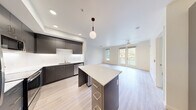 This well-appointed 3-bedroom, 2-bathroom unit at 23040 Military Rd in Kent, WA offers a thoughtfully designed single-level layout with modern finishes throughout. The open-concept kitchen and living area serves as the heart of the home, featuring sleek dark-gray cabinetry, a white quartz-topped island with pendant lighting, stainless steel appliances including a refrigerator, range, and microwave, plus a subway tile backsplash. Light wood-tone flooring runs throughout the main living areas, while the living room is brightened by large windows and glass French doors that open to a private balcony with lush outdoor views. A ceiling fan adds comfort to the living space. The kitchen area also conveniently houses an in-unit stacked washer and dryer behind a louvered closet door. The three bedrooms are carpeted and filled with natural light from large windows, with views of the surrounding neighborhood. The primary bedroom includes a spacious walk-in closet with wire shelving. Both bathrooms are finished with light wood-look flooring, gray vanities, white quartz countertops, and full tub-shower combinations. Two dedicated closets provide ample storage throughout the unit.