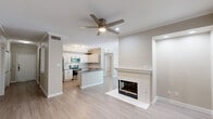 Located in Dallas, TX, this single-floor, 2-bedroom, 2-bathroom residence offers a thoughtfully designed layout with a clean, modern aesthetic. The open-concept living, dining, and kitchen area serves as the heart of the home, anchored by a classic white-mantel fireplace and a ceiling fan with integrated lighting. Light wood-style flooring flows consistently throughout, complementing the neutral warm-beige wall tones and crisp white crown molding. The kitchen is well-equipped with white shaker-style cabinetry, dark quartz countertops, a subway tile backsplash, stainless steel appliances including a range, microwave, and dishwasher, and a peninsula that provides additional workspace and casual seating. A hallway with built-in open shelving connects the main living areas to the bedrooms, adding functional storage. The generously sized primary bedroom features a ceiling fan, crown molding, and a walk-in closet. The second bedroom is equally comfortable, with natural light from a large window and its own ceiling fan. Both bathrooms are finished with white cabinetry, dark countertops, and wood-style flooring. The space also includes a dedicated laundry area and multiple utility and closet spaces, maximizing everyday functionality.
