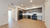 This well-designed 5-bedroom, 2-bathroom unit offers a thoughtful layout spread across a single floor, combining modern finishes with practical functionality throughout. Light-toned luxury vinyl plank flooring flows seamlessly through every room, creating a cohesive and contemporary aesthetic.

The kitchen serves as a central highlight, featuring dark wood-grain cabinetry that extends to the ceiling for ample storage, a marble-style tile backsplash, and a full suite of black appliances including a refrigerator, range, dishwasher, and range hood. Recessed lighting illuminates the space efficiently.

The five bedrooms are bright and neutrally finished, each benefiting from large windows fitted with horizontal blinds that invite natural light while maintaining privacy. Clean white walls and the continuous plank flooring give each room a versatile, move-in-ready feel.

The two bathrooms are finished in a clean, modern style. One features a wood-tone vanity with a marble-look countertop, a mirror, and a full shower-tub combo. The second bathroom is spacious and accessible, with grab bars and a tub-shower combination. Both bathrooms continue the light plank flooring found throughout the unit.

A welcoming entrance, a hallway connecting the rooms, and a dedicated closet round out the layout, ensuring organized and comfortable daily living.