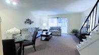 This 3-floor residence offers a well-designed layout that combines comfort and functionality across its multiple levels. The living area serves as a central gathering space, featuring plush wall-to-wall carpeting that adds warmth underfoot. Large sliding glass doors dominate one wall, flooding the room with natural light and providing direct access to an outdoor balcony, where views of surrounding greenery are visible. The generous proportions of the living space comfortably accommodate both a seating arrangement and a dining area, which transitions naturally from the main room. Decorative wall accents add a touch of personality to the neutral, light-toned walls, which contribute to the bright and airy ambiance throughout. The sliding doors are dressed with vertical blinds, allowing for flexible light control. The open-concept design between the living and dining zones encourages a fluid, connected feel, making the space well-suited for both everyday living and entertaining. With three floors in total, the residence provides ample room for varied living arrangements, storage, and private spaces beyond what is visible in the main living area.
