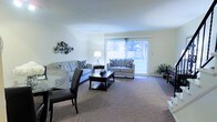 This 3-floor residence offers a well-designed layout that combines comfort and functionality across its multiple levels. The living area serves as a central gathering space, featuring plush wall-to-wall carpeting that adds warmth underfoot. Large sliding glass doors dominate one wall, flooding the room with natural light and providing direct access to an outdoor balcony, where views of surrounding greenery are visible. The generous proportions of the living space comfortably accommodate both a seating arrangement and a dining area, which transitions naturally from the main room. Decorative wall accents add a touch of personality to the neutral, light-toned walls, which contribute to the bright and airy ambiance throughout. The sliding doors are dressed with vertical blinds, allowing for flexible light control. The open-concept design between the living and dining zones encourages a fluid, connected feel, making the space well-suited for both everyday living and entertaining. With three floors in total, the residence provides ample room for varied living arrangements, storage, and private spaces beyond what is visible in the main living area.