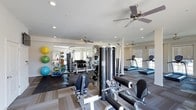 This fitness center is designed to support a comprehensive workout experience within a single, open-plan floor. The space is bright and airy, benefiting from multiple windows that allow natural light to fill the room, complemented by recessed ceiling lighting and several ceiling fans that promote air circulation throughout.

The strength training area is well-stocked, featuring a full dumbbell rack, cable and pulley machines, and a multi-station functional trainer. A dedicated free weights zone includes rubber flooring for safety and durability, along with an assortment of medicine balls, stability balls, and foam rollers neatly organized on wall-mounted racks.

On the cardio side, a row of treadmills lines the windowed wall, offering an energizing view while in use. The layout thoughtfully separates cardio and strength zones, allowing members to move freely without congestion. Neutral-toned flooring with contrasting dark rubber mats helps define each training area and contributes to the clean, modern aesthetic.

The overall ambiance is professional and inviting, with white walls and a consistent design language that keeps the space feeling organized and focused. This fitness center provides everything needed for both strength training and cardiovascular conditioning in a comfortable, well-maintained environment.