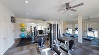 This fitness center is designed to support a comprehensive workout experience within a single, open-plan floor. The space is bright and airy, benefiting from multiple windows that allow natural light to fill the room, complemented by recessed ceiling lighting and several ceiling fans that promote air circulation throughout.

The strength training area is well-stocked, featuring a full dumbbell rack, cable and pulley machines, and a multi-station functional trainer. A dedicated free weights zone includes rubber flooring for safety and durability, along with an assortment of medicine balls, stability balls, and foam rollers neatly organized on wall-mounted racks.

On the cardio side, a row of treadmills lines the windowed wall, offering an energizing view while in use. The layout thoughtfully separates cardio and strength zones, allowing members to move freely without congestion. Neutral-toned flooring with contrasting dark rubber mats helps define each training area and contributes to the clean, modern aesthetic.

The overall ambiance is professional and inviting, with white walls and a consistent design language that keeps the space feeling organized and focused. This fitness center provides everything needed for both strength training and cardiovascular conditioning in a comfortable, well-maintained environment.