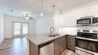 Located at 171 Town Park Dr in Conroe, TX, this one-bedroom, one-bathroom residence offers a thoughtfully designed single-floor layout with modern finishes throughout. The open-concept living area seamlessly combines the dining room, kitchen, and living room, all finished with warm light wood-tone flooring and ceiling fans. The kitchen is a standout feature, showcasing two-tone cabinetry with white upper cabinets and gray lower cabinets, granite countertops, a hexagonal tile backsplash, stainless steel appliances including a refrigerator, range, microwave, and dishwasher, and pendant lighting over the peninsula island with a built-in sink. Natural light flows in through large windows and a door leading to the private balcony. The bedroom is carpeted and bright, featuring a trio of windows with outdoor views and a ceiling fan. It connects directly to the full bathroom, which includes granite-topped gray cabinetry, a wide vanity mirror, wood-look flooring, and a soaking tub with tiled surround. Generous storage is provided by four closets, including a spacious walk-in with multi-tier shelving and hanging rods. An in-unit laundry area completes this functional and stylish home.