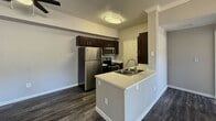 Located at 80 on Gibson, this single-floor apartment offers 810 square feet of functional living space across 2 bedrooms and 4 bathrooms. The kitchen serves as a central highlight, featuring dark espresso cabinetry, stainless steel appliances including a refrigerator, microwave, and range, as well as a peninsula with a built-in sink and light countertops. Dark hardwood-style flooring runs throughout the kitchen and common areas, complementing the neutral gray walls. The bedrooms are carpeted and finished with the same gray color palette, offering a calm and cohesive aesthetic. The primary bedroom measures 140 square feet and includes a ceiling fan, a window for natural light, and a sliding door closet. The secondary bedroom also features a mirrored sliding closet door and ceiling-mounted HVAC vents. The four bathrooms include units with tub-shower combos fitted with chrome fixtures, as well as a vanity bathroom showcasing a vessel sink, dark cabinetry, a large mirror, and a three-light vanity fixture above. White panel doors and clean white baseboards are consistent throughout the unit, contributing to a tidy, well-maintained appearance. Two hallways connect the rooms efficiently across the single-floor layout.