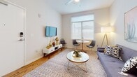 Located at 505 Porter St in Richmond, Virginia, this single-floor residence offers a well-designed layout that balances comfort and modern style. The living area is bright and inviting, featuring hardwood flooring, a large window that admits generous natural light, and a ceiling fan overhead. The space is complemented by a mid-century modern aesthetic, with a wall-mounted TV, a sleek media console, and a cozy seating arrangement centered around a round glass coffee table. A compact dining nook with a round bistro table and contemporary chairs adds functional versatility to the living space. The kitchen is outfitted with stainless steel appliances including a range, microwave, and dishwasher, paired with grey quartz countertops, white cabinetry, and a classic subway tile backsplash that gives the space a clean, polished look. The primary bedroom is softly lit with warm sconce lighting, carpeted flooring, and tasteful wall art, creating a calm and restful atmosphere. A secondary bedroom offers additional flexibility, with carpeted floors, clean white walls, framed artwork, a geometric mirror, and access to a closet or adjoining space. The bathroom features tile flooring, a white vanity with grey countertop, and a shower-tub combo. Throughout, the unit maintains a cohesive, contemporary design with neutral tones and curated décor.