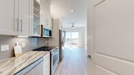 Located at 3500 Cox Rd in Henrico, Virginia, this efficiently designed single-floor unit offers a clean, contemporary aesthetic throughout. Light hardwood flooring flows seamlessly across the entire space, complemented by crisp white walls and recessed lighting that create a bright, airy atmosphere.

The galley-style kitchen is a standout feature, showcasing granite countertops, white shaker-style cabinetry with glass-front upper panels, a subway tile backsplash, and a full suite of stainless steel appliances including a range, built-in microwave, and refrigerator. A built-in counter extension provides additional workspace or casual dining space. The kitchen opens toward a living area illuminated by a large sliding glass door that frames outdoor views and floods the room with natural light. A ceiling fan adds comfort to the living area.

The bathroom is finished with large-format marble-look tile in a glass-enclosed walk-in shower with a built-in niche and brushed nickel fixtures, conveying a polished, upscale feel.

A dedicated walk-in closet features built-in shelving and hanging rods, offering well-organized storage. The overall design is modern, functional, and thoughtfully appointed throughout.