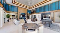Located at 2237 Riley Fuzzel Rd in Spring, TX, this expansive single-floor living space offers an impressive and thoughtfully designed interior. The open-plan layout is anchored by a dramatic double-height ceiling in the main gathering area, accentuated by bold cobalt blue wall panels with dark vertical slat detailing and warm wood trim — a striking architectural feature that defines the space's contemporary character.

Floor-to-ceiling windows and glass sliding doors line the perimeter, flooding the interior with abundant natural light and providing seamless views of the outdoor surroundings. The living room is the heart of the space, featuring multiple distinct seating arrangements that accommodate both relaxed lounging and social interaction. A built-in entertainment wall serves as a focal point, combining wood shelving, dark tile detailing, a large flat-screen display, and a sleek linear electric fireplace framed in vivid blue — a standout design element.

Light-toned large-format tile flooring runs throughout, contributing to the bright, airy ambiance. A game area with a billiard table adds a recreational dimension to the space. Pendant and chandelier lighting fixtures, including a sculptural ring chandelier, provide warm illumination and visual interest. The overall aesthetic blends modern sophistication with inviting comfort, making this a versatile and well-appointed communal living environment.
