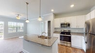 Located at 1300 South Park Way in Sanford, NC, this single-floor home offers a well-designed layout with modern finishes throughout. The kitchen serves as a central highlight, featuring white shaker-style cabinetry, granite countertops, a center island with a undermount sink and pendant lighting, and a full suite of stainless steel appliances including a range, microwave, and refrigerator. Warm hardwood-style flooring completes the kitchen and adjacent living areas.

The bedrooms are carpeted and generously proportioned, each equipped with ceiling fans. Several bedrooms benefit from natural light through windows with blinds, offering views of the surrounding neighborhood. One bedroom includes access to a walk-in closet outfitted with wire shelving systems, providing practical storage solutions.

The bathrooms are finished with tile flooring, dark espresso-toned vanities topped with granite countertops, and brushed nickel hardware. A full bathroom includes a soaking tub and shower combination, while a secondary bathroom functions as a half bath. Soft neutral tones in a cool sage-gray palette flow consistently throughout the home, contributing to a clean, cohesive aesthetic. The floor plan is efficiently organized, making the most of its single-level layout.
