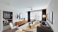 This single-floor, two-bedroom, two-bathroom residence offers a thoughtfully designed layout with a cohesive contemporary aesthetic. The living room serves as a welcoming central space, featuring hardwood-style flooring, a ceiling fan, and large windows fitted with blinds and dark drape panels that frame views of the surrounding urban environment. Natural light fills the room, complementing its neutral palette.

The kitchen is a standout feature, showcasing floor-to-ceiling dark cabinetry, granite-style countertops, a tile backsplash, and a full suite of stainless steel appliances including a range, microwave, and refrigerator. Track lighting overhead adds a polished, functional touch. An island with a sink provides additional workspace and storage.

The primary bedroom is distinguished by a deep slate-blue accent wall, ceiling fan, plush carpeting, and a window with natural light. The en-suite bathroom offers dual vanity sinks with granite countertops, dark cabinetry, hardwood-style flooring, and access to a walk-in closet. The second bedroom features neutral tones and natural light, with an adjacent full bathroom finished in consistent materials. A dedicated office space with dark accent walls and natural light completes this well-rounded residence.