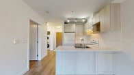 Located at 1408 E 15th Ave in Vancouver's vibrant Kensington-Cedar Cottage neighbourhood, this one-bedroom, one-bathroom unit offers a thoughtfully designed single-floor layout. The open-concept living, dining, and kitchen area forms the heart of the home, bathed in natural light through large floor-to-ceiling windows that frame lush green outdoor views. The kitchen is equipped with light wood cabinetry, a white appliance package including a refrigerator, electric range, and dishwasher, a stainless steel sink, light countertops, and a tiled backsplash — all finished in a clean, contemporary style. Warm wood-tone laminate flooring flows throughout the unit, adding continuity and warmth to the bright, white interior. The well-proportioned bedroom includes built-in closet storage and a large window overlooking the surrounding greenery. An additional den provides flexible space suitable for a home office or secondary sleeping area. A full bathroom features a tub-shower combo with white subway-style tiling. In-unit stacked laundry is conveniently tucked behind a dedicated closet door. Two additional closets offer ample storage. The unit's modern, neutral palette and efficient layout make it a functional and comfortable urban residence.