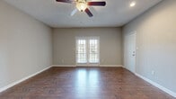 Located at 1290 W Government St in Brandon, MS, this single-story, 3-bedroom, 2-bathroom home offers a well-designed open-concept layout with consistent, warm hardwood-style flooring throughout the main living areas. The expansive living room is a highlight, featuring a ceiling fan with light fixture, a textured ceiling, neutral gray-toned walls, and a set of French doors that invite natural light and provide outdoor access. The living area flows seamlessly into the kitchen and dining space, where rich dark wood cabinetry pairs with granite-style countertops and a breakfast bar with decorative iron corbels. The kitchen is equipped with stainless steel appliances, including a range, microwave, refrigerator, and dishwasher, offering both style and functionality. The two bathrooms continue the cohesive design with matching dark cabinetry and granite countertops, with one bathroom featuring a tub-shower combination. The three bedrooms are carpeted for comfort; the generously sized primary bedroom offers ample space, while the additional bedrooms include dual closets, maximizing storage. Overall, the home presents a clean, modern aesthetic with a neutral palette throughout, creating a bright and functional living environment.