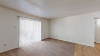 This single-floor residence offers a practical and comfortable layout encompassing one bedroom, two bathrooms, a living room, kitchen, and a dedicated closet. The living room is a welcoming space featuring plush wall-to-wall carpeting, neutral walls, and a textured ceiling. A full-length vertical blind-covered sliding glass door floods the room with natural light while offering views of surrounding greenery. The transition to hardwood-style flooring near the entry adds a clean visual contrast.

The kitchen is efficiently laid out in a galley style, featuring dark wood cabinetry, granite-toned countertops, a double stainless steel sink, and white appliances including a refrigerator and dishwasher. Light wood-style flooring ties the space together with a bright, clean aesthetic.

The carpeted bedroom is a comfortably sized retreat with a window that frames outdoor tree views and provides ample natural light. It connects to a generously sized walk-in closet outfitted with dual hanging rods and a central shelving unit, offering substantial storage capacity.

The two bathrooms include a full bath featuring a white tile tub-shower combo with chrome fixtures and wood-style flooring, and a second bathroom with an extended vanity countertop paired with a large mirror. Textured ceilings are consistent throughout the home, contributing to its classic residential character.