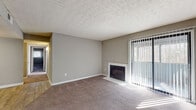 This single-floor residence presents a well-organized layout with distinct living, sleeping, and functional zones. The living room serves as a central gathering space, highlighted by a fireplace with a clean white surround and a large sliding glass door fitted with vertical blinds, allowing natural light to pour in while offering outdoor access and views of surrounding greenery. Soft carpeting and neutral gray walls carry throughout the living area, creating a calm, cohesive atmosphere.

The bedrooms are generously sized, each featuring plush carpeting, neutral-toned walls, and windows with blinds that provide natural light and privacy. One bedroom includes two closets — a standard door closet and a bi-fold closet — offering ample storage. An adjacent area with wood-look flooring connects seamlessly to the bedroom spaces.

The kitchen is equipped with dark cabinetry, light countertops, and a black electric range with overhead ventilation, providing a functional and efficient cooking space.

The bathroom features wood-look flooring, a dark wood vanity with a light countertop, a framed mirror, and a full tub-shower combination with white tile surround. Textured ceilings are consistent throughout, adding a classic residential character to the overall space.