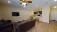 Located at 3607 University Blvd N in Jacksonville, FL, this single-floor unit offers a well-designed, open-concept layout that seamlessly connects the living and kitchen areas. The living room is generously sized, featuring durable hardwood-style flooring, recessed lighting, a ceiling fan, and French doors that invite natural light and provide outdoor access. The kitchen is a standout feature, equipped with dark espresso cabinetry, granite countertops, stainless steel appliances including a range, microwave, and refrigerator, and a peninsula breakfast bar with seating — ideal for casual dining and entertaining. Pendant lighting adds a refined touch above both the bar and kitchen workspace. The bedrooms are carpeted for comfort, each outfitted with ceiling fans and windows that bring in natural light. At least one bedroom includes an en-suite bathroom access. The bathroom features wood-style tile flooring, a tub-shower combination with tile surround, a vanity with dark cabinetry, and neutral wall tones. Throughout the unit, warm beige walls, clean white trim, and consistent flooring choices create a cohesive and inviting atmosphere well-suited for everyday living.