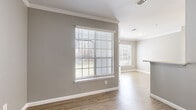 This single-floor, 2-bedroom, 1-bathroom residence offers a thoughtfully designed layout that makes efficient use of its space. The open-concept living, dining, and kitchen area serves as the heart of the home, finished with light hardwood-style flooring and neutral gray walls accented by crisp white crown molding and baseboards. Large windows fitted with horizontal blinds allow generous natural light throughout the common areas.

The kitchen is well-equipped with stainless steel appliances — including a refrigerator, range, and microwave — complemented by white shaker-style cabinetry, a gray subway tile backsplash, and light quartz countertops extending to a breakfast bar peninsula.

The primary bedroom offers a spacious walk-in closet with built-in wire shelving and carpeted flooring, while a secondary bedroom features hardwood-style flooring and a large window with outdoor views. The entry hallway includes built-in open shelving, adding practical storage. The bathroom is cleanly finished with a white vanity, quartz countertop, lighted mirror, and wood-look tile flooring. A ceiling fan is present in the living area, and crown molding details are carried through the main living spaces, contributing to a cohesive and polished overall aesthetic.