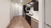 This well-appointed single-floor unit offers a thoughtfully designed layout that balances functionality with modern style. The kitchen is a standout feature, showcasing rich dark espresso cabinetry, crisp white countertops, a stainless steel sink, and a full suite of stainless steel appliances including a range, microwave, refrigerator, and dishwasher. Recessed lighting and durable hardwood-style flooring carry throughout the space, lending a clean, contemporary feel.

The living area is open and airy, benefiting from a sliding glass door that provides direct outdoor access and allows natural light to pour in. A ceiling fan adds comfort to the space, while an additional window further brightens the room and offers views of the surrounding area.

The hallway connects the main living spaces to the bedroom and bathrooms with ease. The primary bathroom is generously sized, featuring large-format tile flooring, a soaking tub with a tiled surround, and an extended vanity with dark cabinetry, white countertops, and a framed mirror illuminated by a well-placed light bar. A secondary bathroom is also accessible, featuring tile flooring and a toilet. Throughout the unit, clean white walls and neutral finishes create a cohesive, move-in-ready aesthetic.
