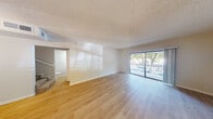This two-story residence offers five bedrooms and three bathrooms thoughtfully distributed across two floors. The ground floor, which serves as the primary living area, features an open living room finished with light hardwood-style flooring and a textured ceiling. A sliding glass door opens to a balcony, allowing natural light to fill the space and providing outdoor views of surrounding trees. Adjacent to the living room, the dining area is defined by a modern chandelier and connects directly to the kitchen through a pass-through counter. The kitchen is equipped with white shaker-style cabinetry, granite countertops, a subway tile backsplash, and stainless steel appliances including a range and over-the-range microwave. The upper floor houses the majority of the bedrooms, including the generously sized primary bedroom, all carpeted and fitted with windows that bring in natural light. Closets with built-in shelving provide practical storage. The three bathrooms are finished consistently with granite-topped white vanities, framed mirrors, and tub-shower combinations with hardwood-style flooring, reflecting a clean and cohesive design throughout.