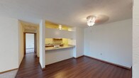 Located in Columbia, IL, this single-floor unit offers a well-organized layout designed for comfortable everyday living. The open-concept living and dining area is finished with rich, dark hardwood-style flooring that extends throughout the main living space, creating a warm and cohesive atmosphere. A ceiling light fixture with a pull-chain fan anchors the room, while recessed lighting adds supplemental illumination near the entryway.

The kitchen is positioned behind a half-wall pass-through counter, providing a functional separation while maintaining an open feel. It is equipped with warm wood cabinetry, a white refrigerator, an electric range with oven, and ample counter space finished in a neutral laminate. Tile-style flooring in the kitchen area offers easy maintenance. Under-cabinet lighting enhances the workspace and adds a subtle glow to the area.

The bedroom features plush carpeting, a closet with sliding wood-panel doors, and direct access to the hallway. The full bathroom includes a single-sink vanity with wood cabinetry, a large mirror with overhead strip lighting, a toilet, and a full-size tub and shower combination. The unit also features a closet near the entryway, adding practical storage to the overall floor plan.