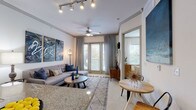 This single-story residence on Marathon Ave in Richardson, TX, offers a thoughtfully designed interior with a cohesive contemporary aesthetic. The living area serves as the heart of the home, featuring a ceiling fan, track lighting, and floor-to-ceiling French doors that invite abundant natural light and views of the surrounding greenery. Crown molding adds a refined architectural touch, while a large sectional sofa, layered textiles, and bold abstract wall art create a welcoming and visually dynamic atmosphere.

The kitchen is outfitted with dark cabinetry extending to the ceiling, stainless steel appliances including a refrigerator and microwave, a black range, and a tile backsplash. Wood-look flooring grounds the space and contrasts cleanly with the dark finishes.

The bedrooms are carpeted and well-lit by natural light from large windows with blinds and draping curtains. Each room offers a calm, neutral palette. The primary bedroom features an exterior-facing window with outdoor views, while the secondary bedroom includes decorative wall accents and warm ambient lighting.

The bathroom features tile flooring, dark vanity cabinetry with granite countertops, and a well-lit mirror. A dedicated laundry closet is also accessible from the bathroom corridor, adding everyday convenience to this well-rounded residence.