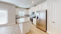 Located at 910 Simmons Dr in Moore, South Carolina, this two-story home is designed with a clean, modern aesthetic and thoughtful finishes throughout. The kitchen serves as a standout feature, showcasing crisp white shaker cabinetry, granite countertops, a tile backsplash, a central island, and a full suite of stainless steel appliances including a French door refrigerator, range, microwave, and dishwasher. Light hardwood-style flooring runs through the main living areas, complemented by recessed lighting and a ceiling fan. A dining area adjacent to the kitchen is brightened by French doors that invite natural light and provide outdoor access. The primary bedroom features a tray ceiling with crown molding, a ceiling fan, plush carpeting, and windows overlooking the exterior. Its en-suite bathroom offers a walk-in shower with glass sliding doors, a vanity with granite countertops, white cabinetry, and warm hardwood-style flooring. Additional bedrooms are carpeted and receive abundant natural light through blinds-fitted windows. A secondary bathroom includes a tub-shower combination, granite vanity, white cabinetry, and matching flooring. The home's neutral palette and consistent finishes create a cohesive, move-in-ready atmosphere throughout both floors.