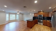 Located at Fairfield Broadway Knolls at Holbrook in Holbrook, NY, this single-floor residence offers a well-designed open-concept layout that seamlessly connects the kitchen and living areas. The kitchen is a standout feature, showcasing rich warm-toned wood cabinetry, sleek dark granite countertops with a matching backsplash, and a full suite of stainless steel appliances including a side-by-side refrigerator with water dispenser, electric range, built-in microwave, and dishwasher. A kitchen island with pendant lighting above provides additional prep and seating space. Crown molding runs throughout the main living areas, adding a refined architectural touch, while recessed lighting and ceiling fans ensure comfort and functionality. The living area is finished with warm hardwood-style flooring that extends throughout the open space, complemented by natural light from windows with blinds. The bedroom features plush carpeting, crown molding, and a ceiling fan. The bathrooms are appointed with dark granite-topped vanities, rich wood cabinetry, and tile flooring. One bathroom includes a tub-shower combination with glass sliding doors, while the other features a stall shower setup. The overall design balances practicality with tasteful finishes throughout.