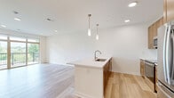 This thoughtfully designed 1-bedroom, 1-bathroom residence in Menomonee Falls, WI offers a functional and modern open-concept layout. Light-toned hardwood flooring flows throughout the main living areas, lending a clean, contemporary feel to the space.

The combined kitchen and living area serves as the heart of the home. The kitchen is equipped with warm-toned wood cabinetry, stainless steel appliances including a refrigerator, microwave, and range, a subway tile backsplash, and a large white quartz island with an undermount sink and pendant lighting overhead. The living area opens directly onto a private balcony through expansive sliding glass doors framed in wood, offering picturesque views of lush greenery and landscaped grounds.

The spacious bedroom features plush neutral carpeting, a ceiling fan with light fixture, and a window that brings in natural light with outdoor views. It includes a dedicated walk-in closet with built-in shelving for ample storage.

The bathroom is finished with warm wood cabinetry, a white quartz double-sink vanity, a large wall mirror with overhead lighting, and a glass-enclosed walk-in shower, all complemented by light wood-look tile flooring. The overall ambiance of this residence is bright, clean, and modern.