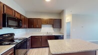 This single-floor unit offers a thoughtfully designed layout that balances functionality and modern aesthetics. The kitchen serves as a central highlight, featuring rich dark-toned cabinetry with brushed nickel hardware and light granite countertops that extend to a peninsula island, providing additional prep and dining space. Black appliances, including a refrigerator, electric range with over-the-range microwave, and dishwasher, complete the kitchen's cohesive look. Light hardwood-style flooring runs throughout the main living areas and bedrooms, contributing to a clean, contemporary feel.

The open living area is spacious and bright, benefiting from large windows that allow natural light to fill the room, with a ceiling fan overhead for added comfort. A corridor connects the living and sleeping areas, with access to a generously sized walk-in closet featuring built-in wire shelving on multiple walls.

Two bathrooms are present: one includes a soaking tub and shower combination framed by white subway tile, while the second offers a glass-enclosed walk-in shower with matching subway tile. Both bathrooms feature granite-topped dark vanities and light tile flooring, maintaining a consistent and polished design throughout the unit.