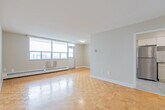 Located at 100 Queen St N in downtown Kitchener, this one-bedroom, one-bathroom unit offers a well-organized layout across a comfortable single floor. The living room is a standout space, featuring warm parquet flooring and expansive windows that frame elevated city views and flood the room with natural light. Baseboard heating runs along the exterior walls, complementing the bright, neutral palette throughout.

The kitchen has been thoughtfully updated with white shaker-style cabinetry, a classic subway tile backsplash, light tile flooring, and a full suite of stainless steel appliances, including a refrigerator and electric range. The entrance foyer provides a clean transition into the living area, finished with the same light tile as the kitchen.

The bedroom is a generously sized retreat with its own large window dressed with vertical blinds, parquet flooring, and a double-door closet offering ample storage. The bathroom features a tub-shower combination with white subway tile surround, an accent tile border, and a safety grab bar. Throughout the unit, neutral tones and clean finishes create a bright, functional living environment well-suited to everyday comfort.