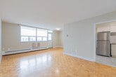 Located at 100 Queen St N in downtown Kitchener, this one-bedroom, one-bathroom unit offers a well-organized layout across a comfortable single floor. The living room is a standout space, featuring warm parquet flooring and expansive windows that frame elevated city views and flood the room with natural light. Baseboard heating runs along the exterior walls, complementing the bright, neutral palette throughout.

The kitchen has been thoughtfully updated with white shaker-style cabinetry, a classic subway tile backsplash, light tile flooring, and a full suite of stainless steel appliances, including a refrigerator and electric range. The entrance foyer provides a clean transition into the living area, finished with the same light tile as the kitchen.

The bedroom is a generously sized retreat with its own large window dressed with vertical blinds, parquet flooring, and a double-door closet offering ample storage. The bathroom features a tub-shower combination with white subway tile surround, an accent tile border, and a safety grab bar. Throughout the unit, neutral tones and clean finishes create a bright, functional living environment well-suited to everyday comfort.